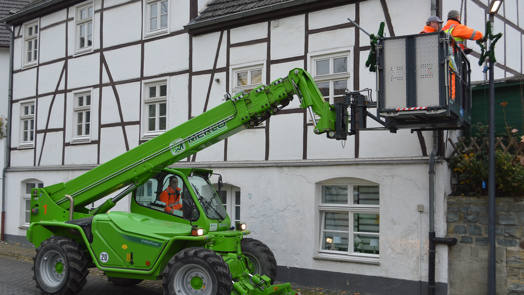 Vergrößerung des Bildes für Ein Teleskoplader mit Arbeitsplattform, auf der zwei Arbeiter stehen, die Arbeiten an einer Hausfassade ausführen möchten..