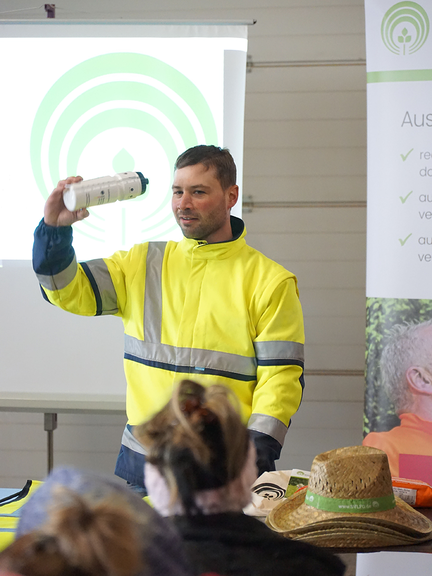 Trinkflasche Vergrößerung des Bildes für Ein Mann hält eine Trinkflasche vor einer Gruppe von Saisonarbeitskräften in die Höhe..